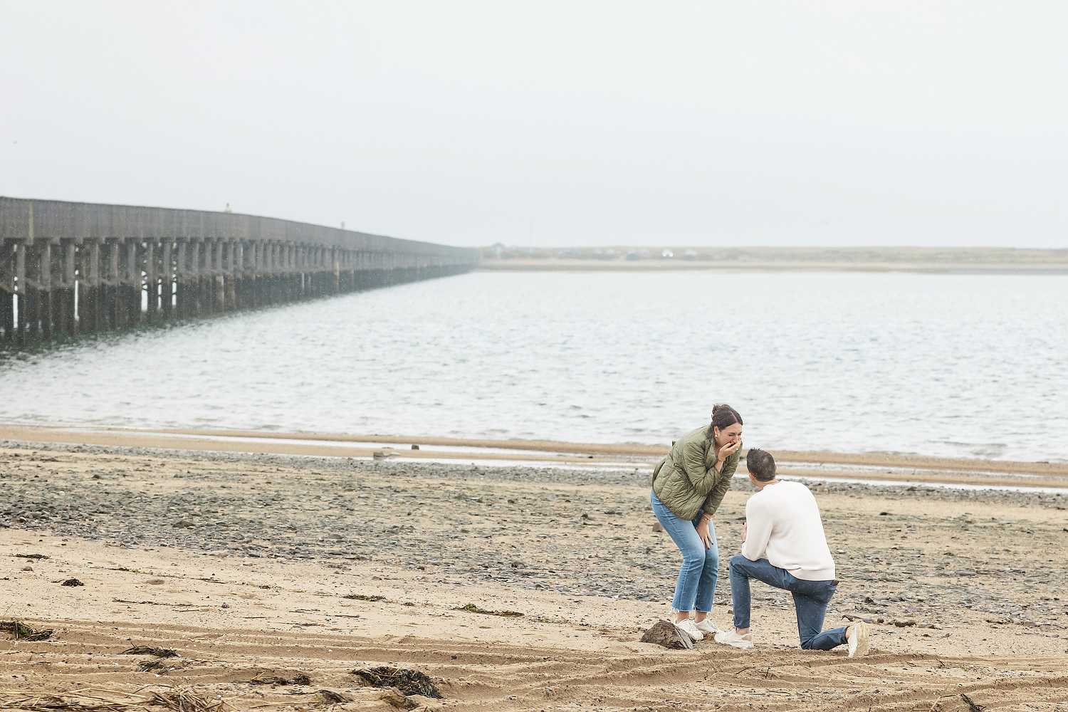 Couple embracing during surprise proposal on rainy Duxbury Beach tidal flats