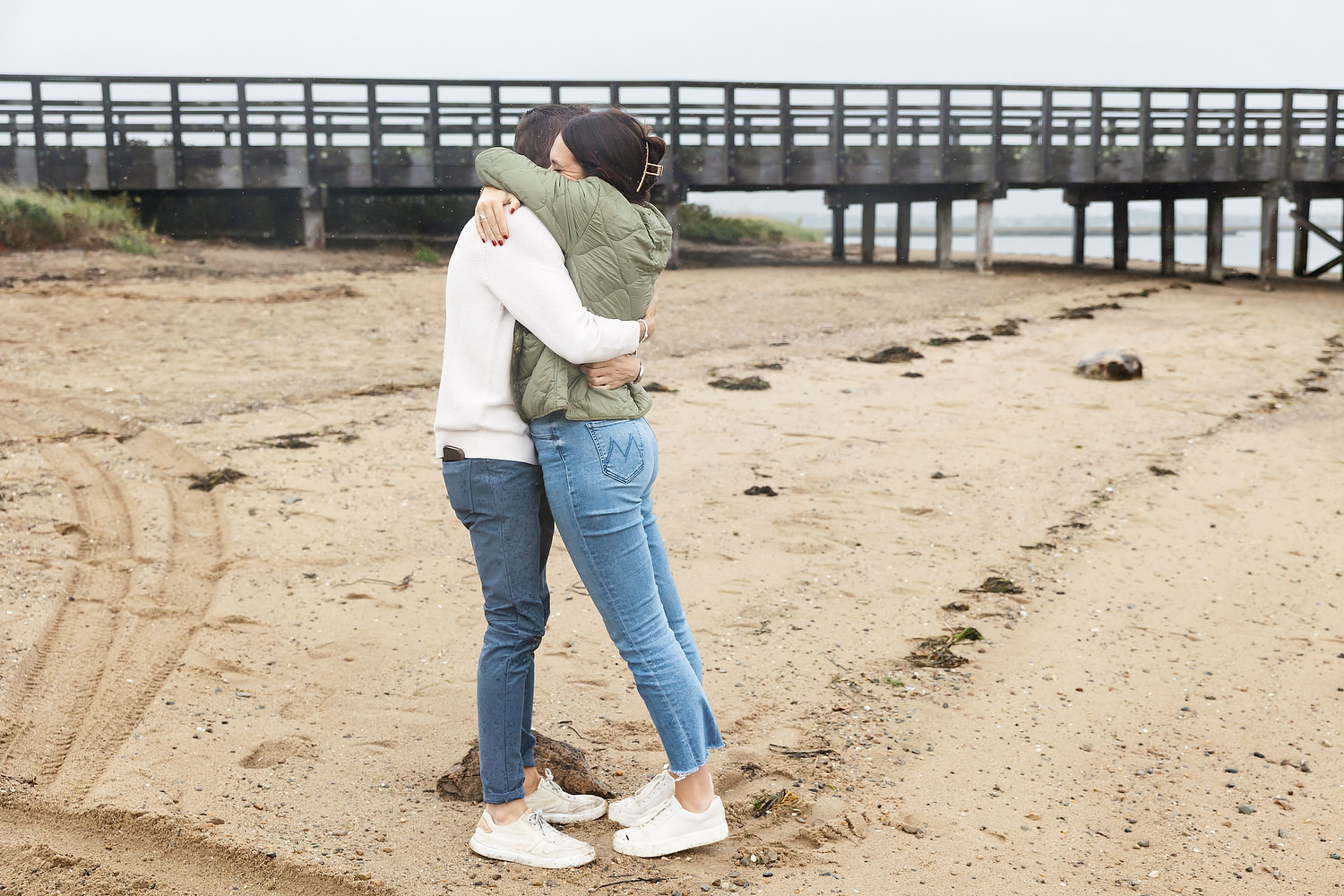 Groom down on one knee in wet sand at Duxbury Beach with ocean in the background