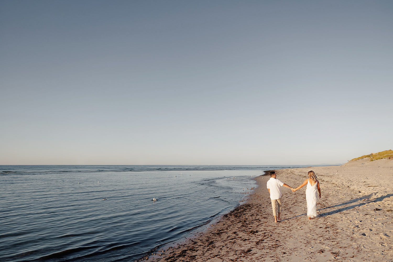 Couple walking barefoot across tidal flats during golden-hour engagement at Mayflower Beach