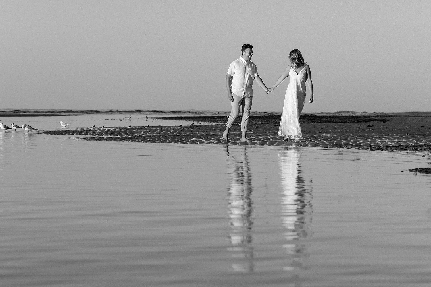 Wide view of couple standing on mirrored sand at Mayflower Beach