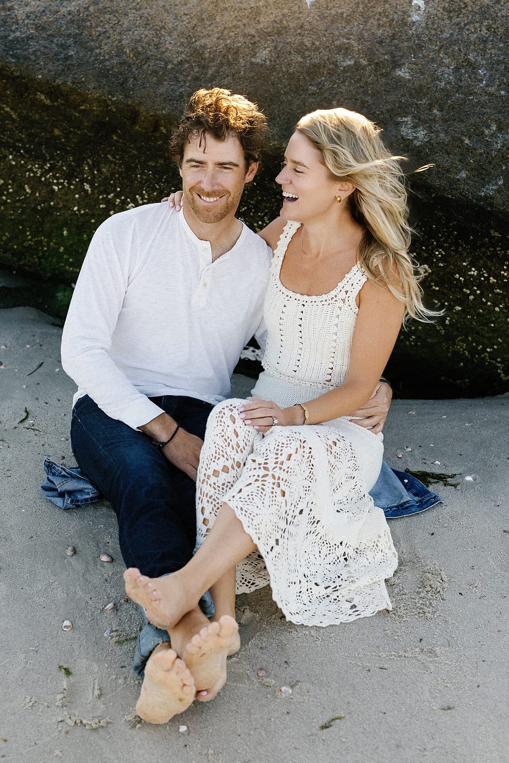 Close-up of couple laughing with beach and shoreline behind them